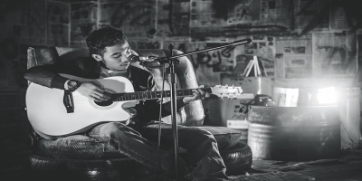 A singer sitting and playing an acoustic guitar in front of a microphone