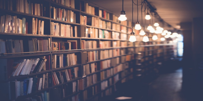 Long rows of library shelves filled with books and lit by hanging lights